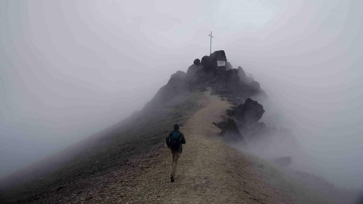 A lone hiker heads towards a cross at the top of a peak of as the fog clears on Guagua Pichincha