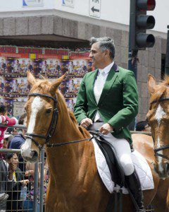 A man in traditional riding clothes including a green hunting jacket on a roan horse