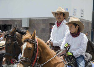 Father and son in matching white shirts, red bandanas, and straw cowboy hats ride in the Caceria del Zorro parade