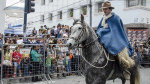 Traditional guacho in wool cowboy hat, blue wool poncho, and alpaca chaps rides a mottled gray and white horse