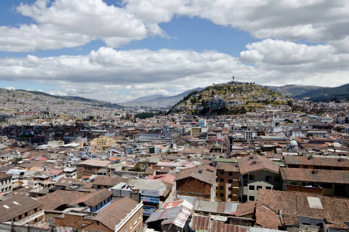 La ciudad de Quito, Ecuador con tejados en primer plano, el Panecillo (una cima redondeada) en el fondo y cielos azules