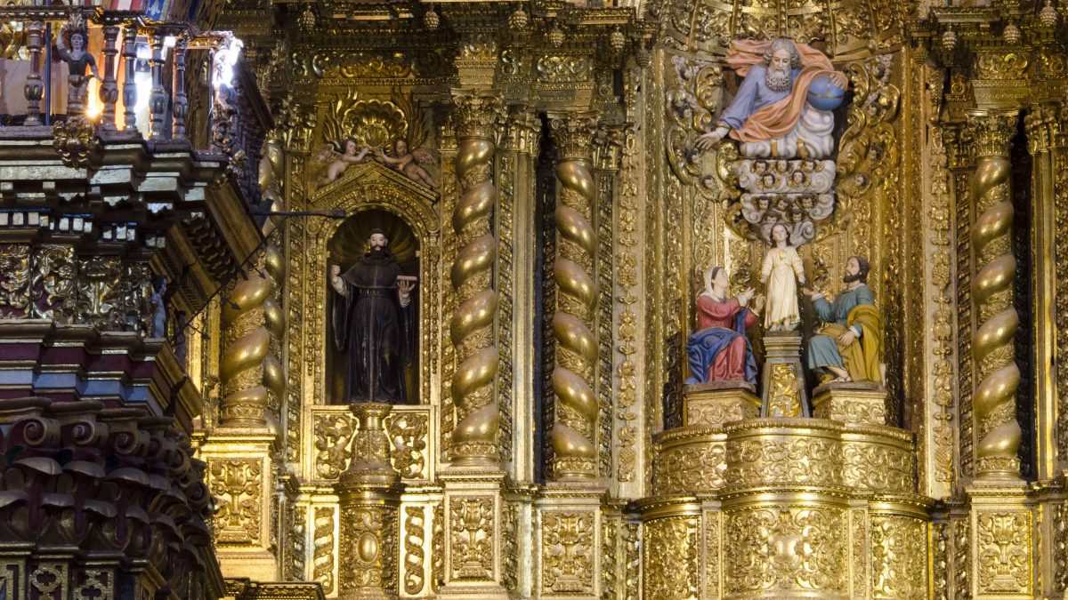 The front altar of La Compania de Jesus includes an painted statue of God in a blue gown and pink robe looking down on the child Jesus flanked by his kneeling parents, Mary and Joseph