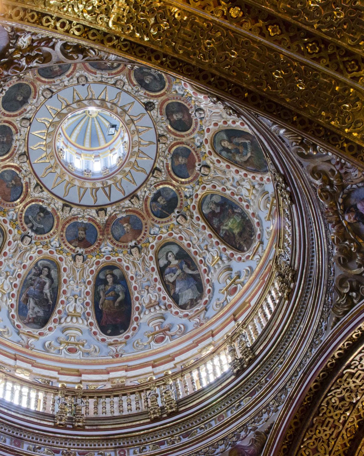 Looking up at the central dome in tones of light blue, dark portraits, and gold trim