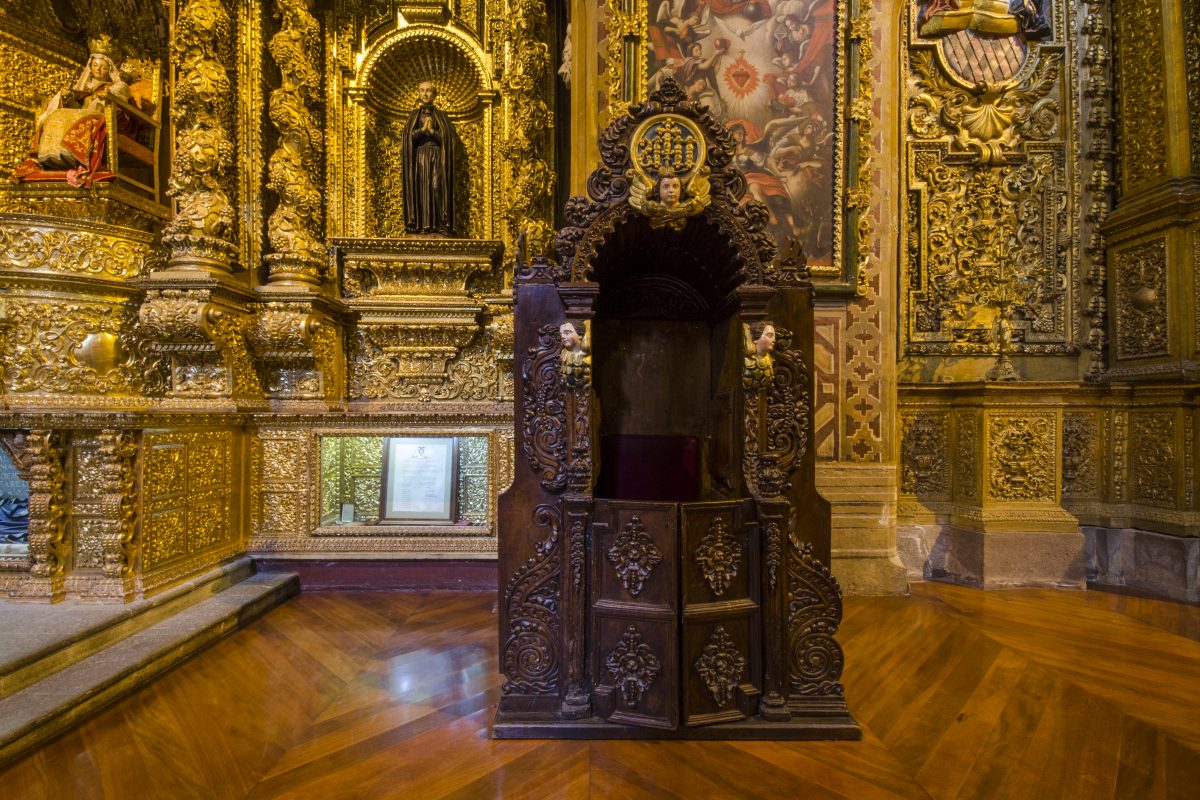 Una confesión de madera oscura destaca contra paredes cubiertas con pan de oro