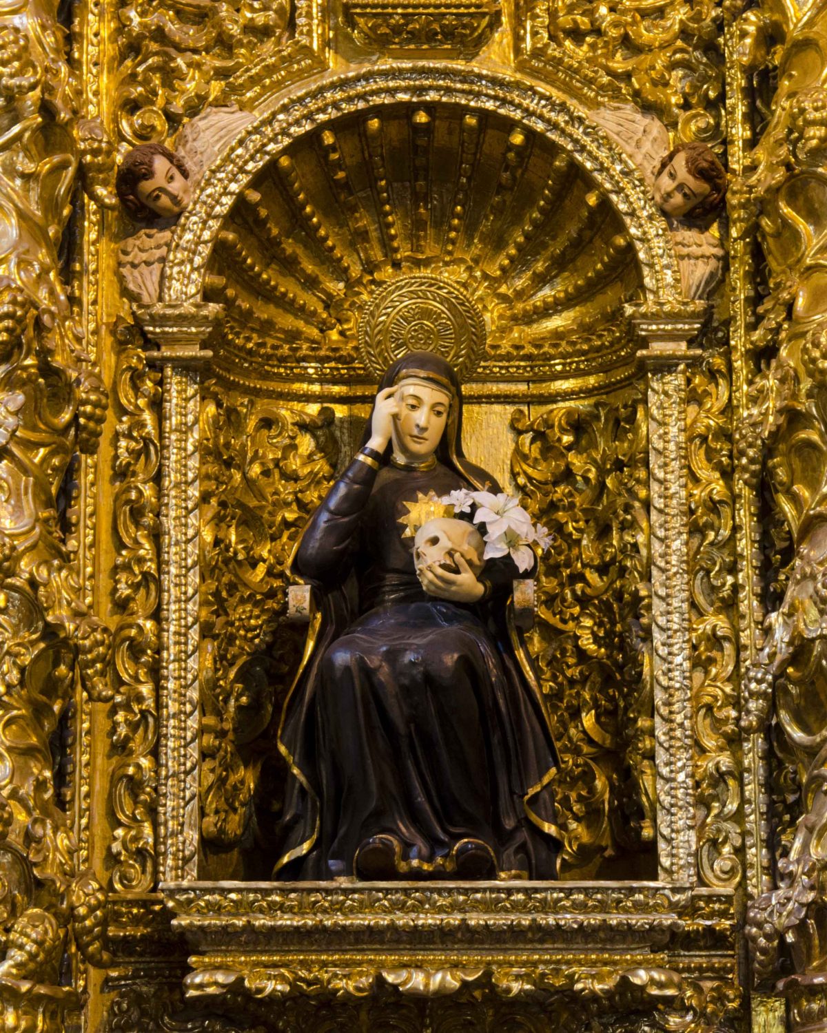 Mariana de Jesús, la patrona de Quito; La Compañía de Jesús, vestida con túnicas negras, sentada sosteniendo una calavera y lirios, rodeada de detalles dorados | ©Ángela Drake