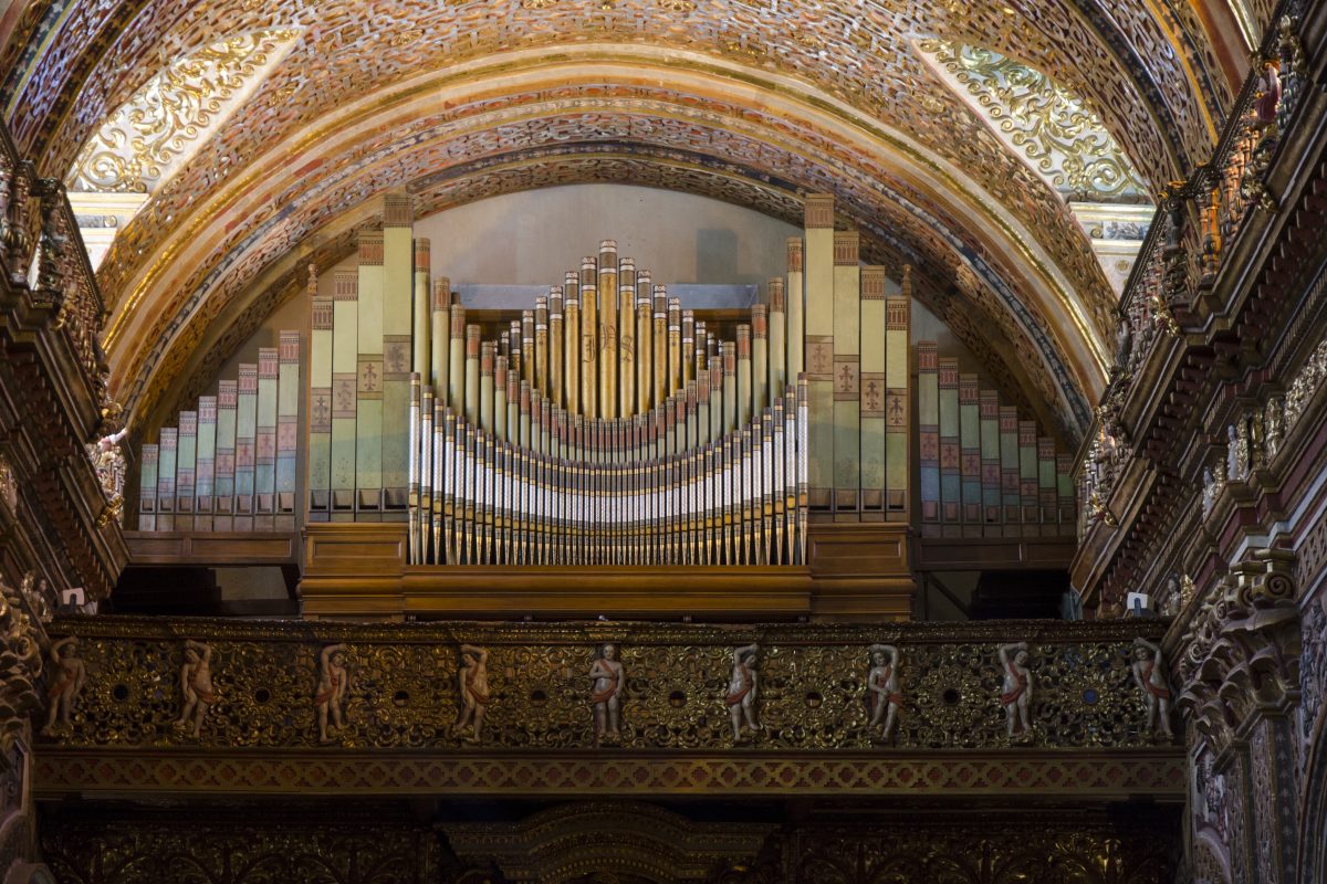 An intricate organ in gold and silver sits below an archway in the choirstall below 