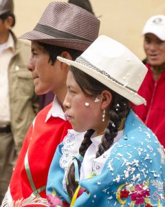 Man dressed in red poncho and brown felt hat walks beside womand dressed in light blue poncho with white Panama hat