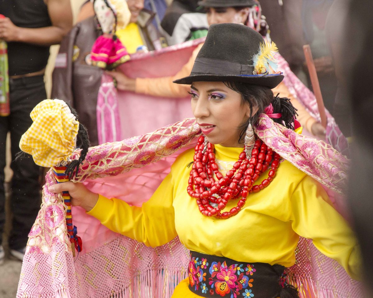 Bailarina vestida con camisa amarilla brillante, chal rosa y collar rojo pesado también usa un sombrero de fieltro marrón oscuro, Carnaval en Guamote