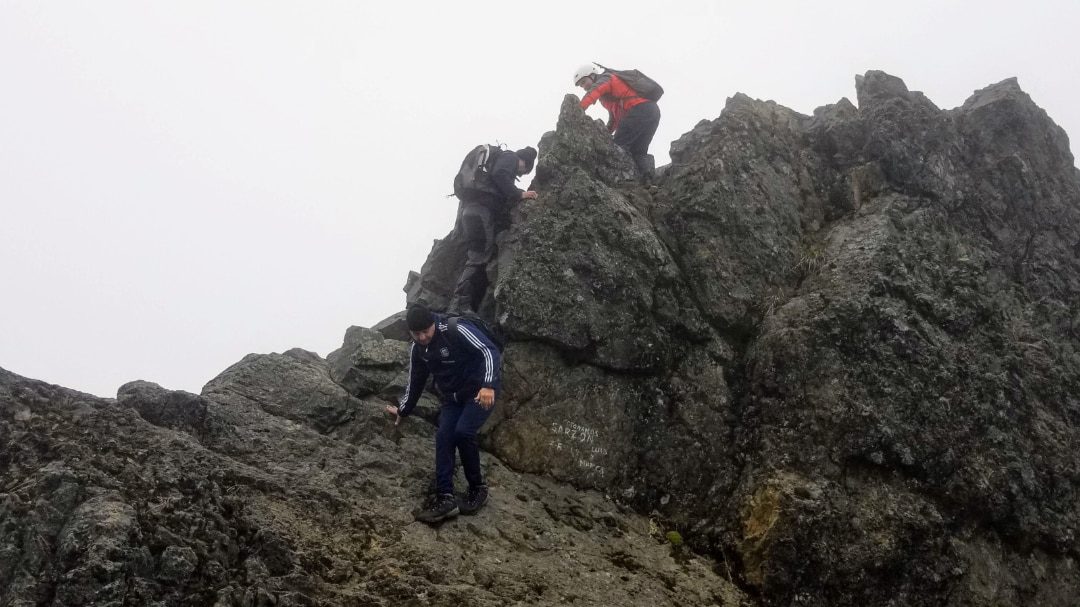 Un excursionista ayuda a otro a subir a la cima del Rucu Pichincha
