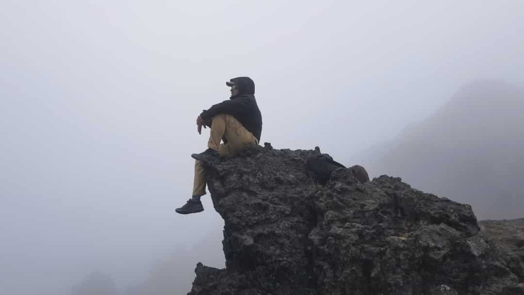 El autor sentado en la punta de una cresta con vistas a la niebla