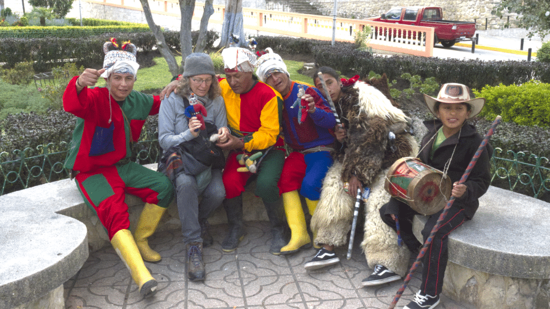 Author sitting on bench between men dressed in colorful costumes 