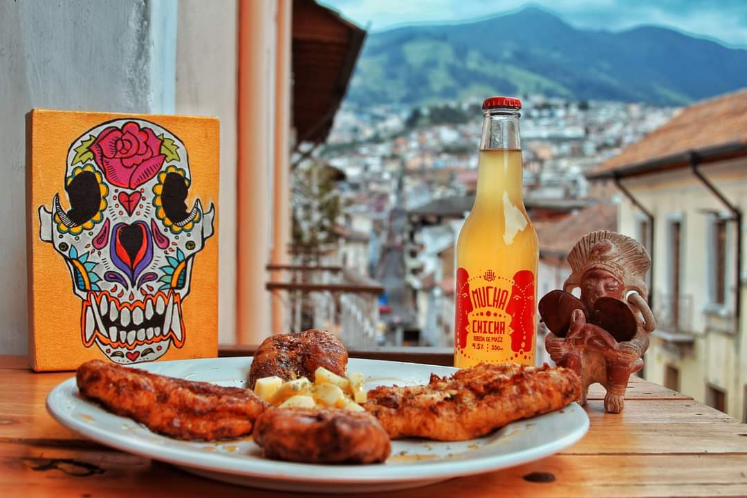 Plate of food, bottle of chicha, and view of historic Quito
