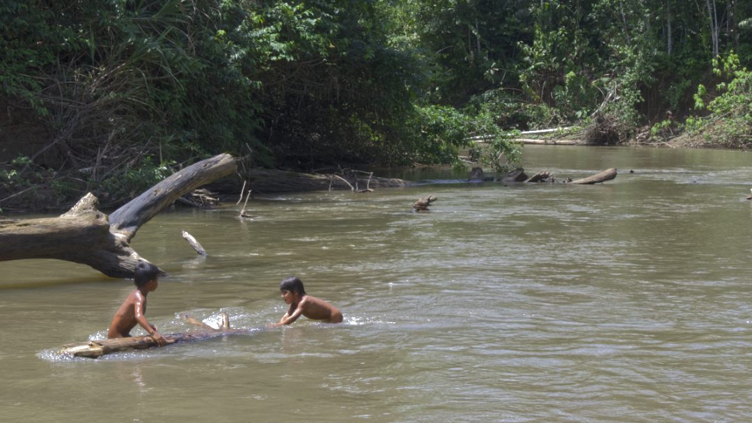 two naked children, lower bodies submersed in water, play in the shallow river