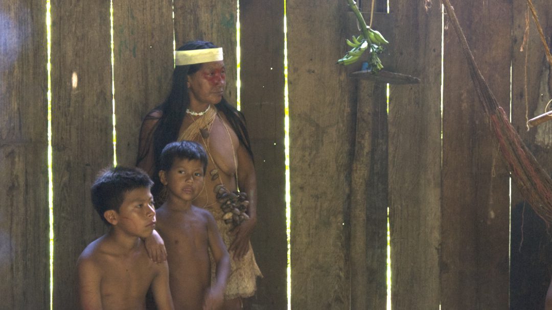 Una mujer Huaorani en clase tradicional y dos jóvenes Huaorani con el pecho desnudo