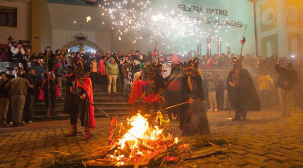 People dressed as devils stand around a fire in the center of a church plaza in Alangasi, Ecuador