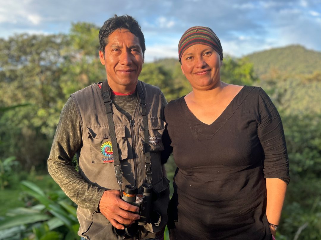 An Ecuadorian couple, man and woman, stand arm in arm, smiling at the camera