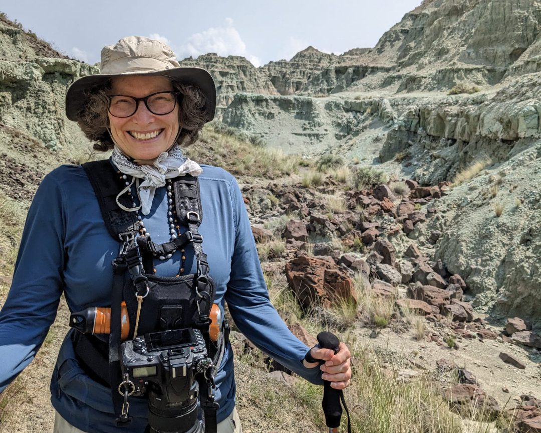 Woman wearing camera and hiking gear poses for camera with a huge smile on her face