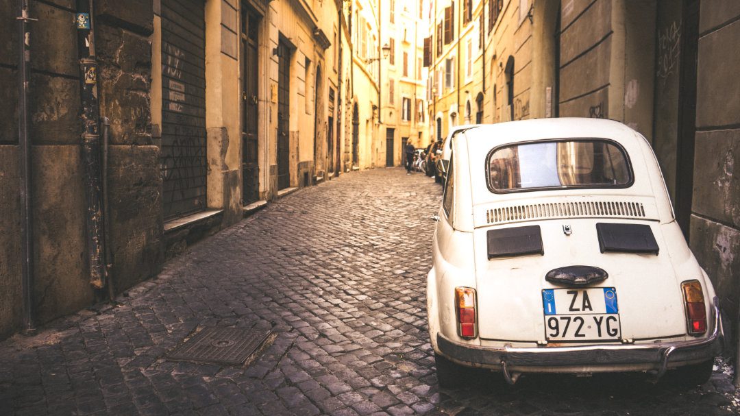 Vintage white car parked on cobblestone streets.
