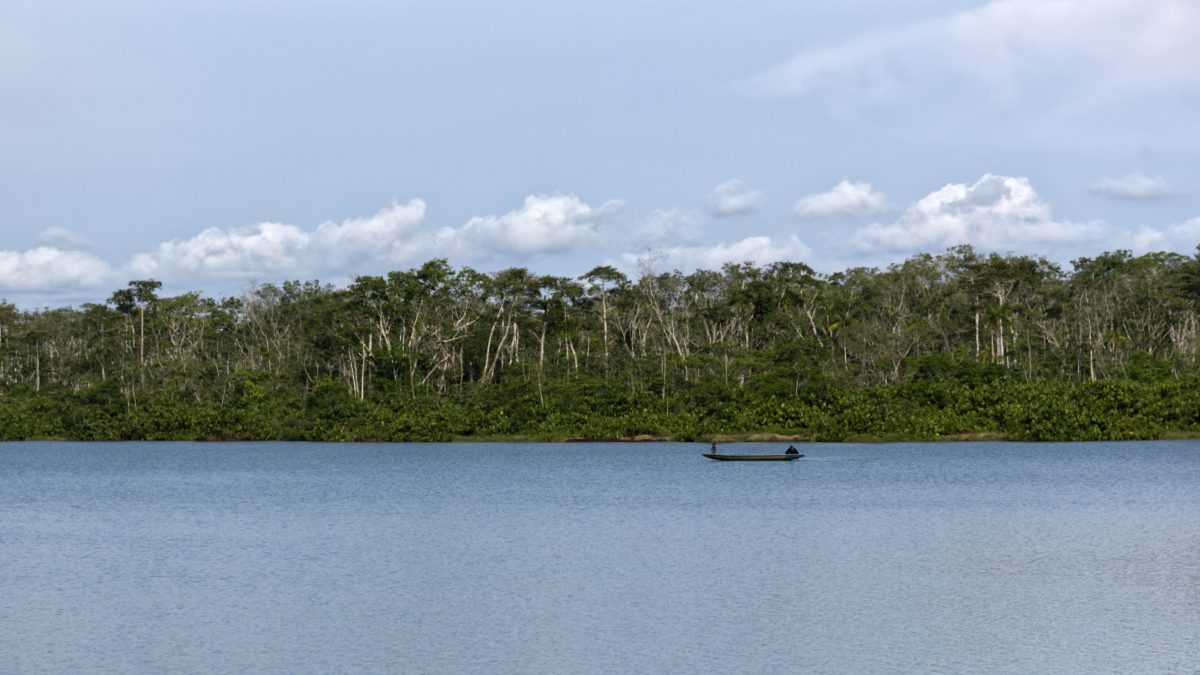 A single, non-motorize canoe sits atop a blue lake bordered by dark green forest on a partly cloudy day.