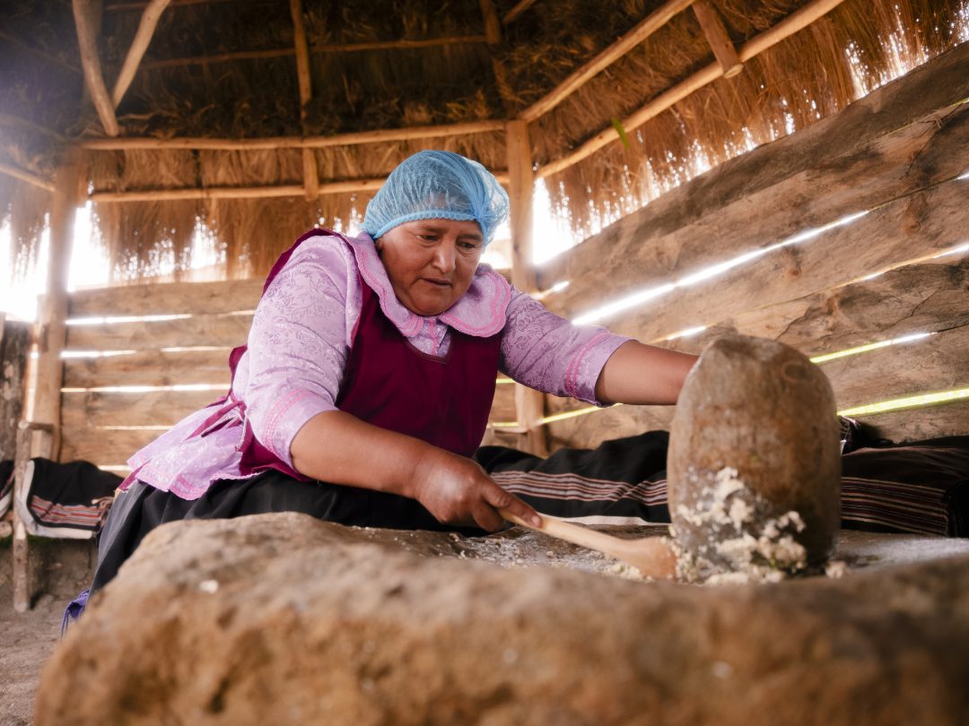 A woman grinds fresh corn in a large stone.