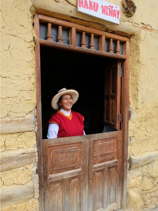 Woman greets unseen guests while standing framed within a half open doorway in San Jose, Peru.