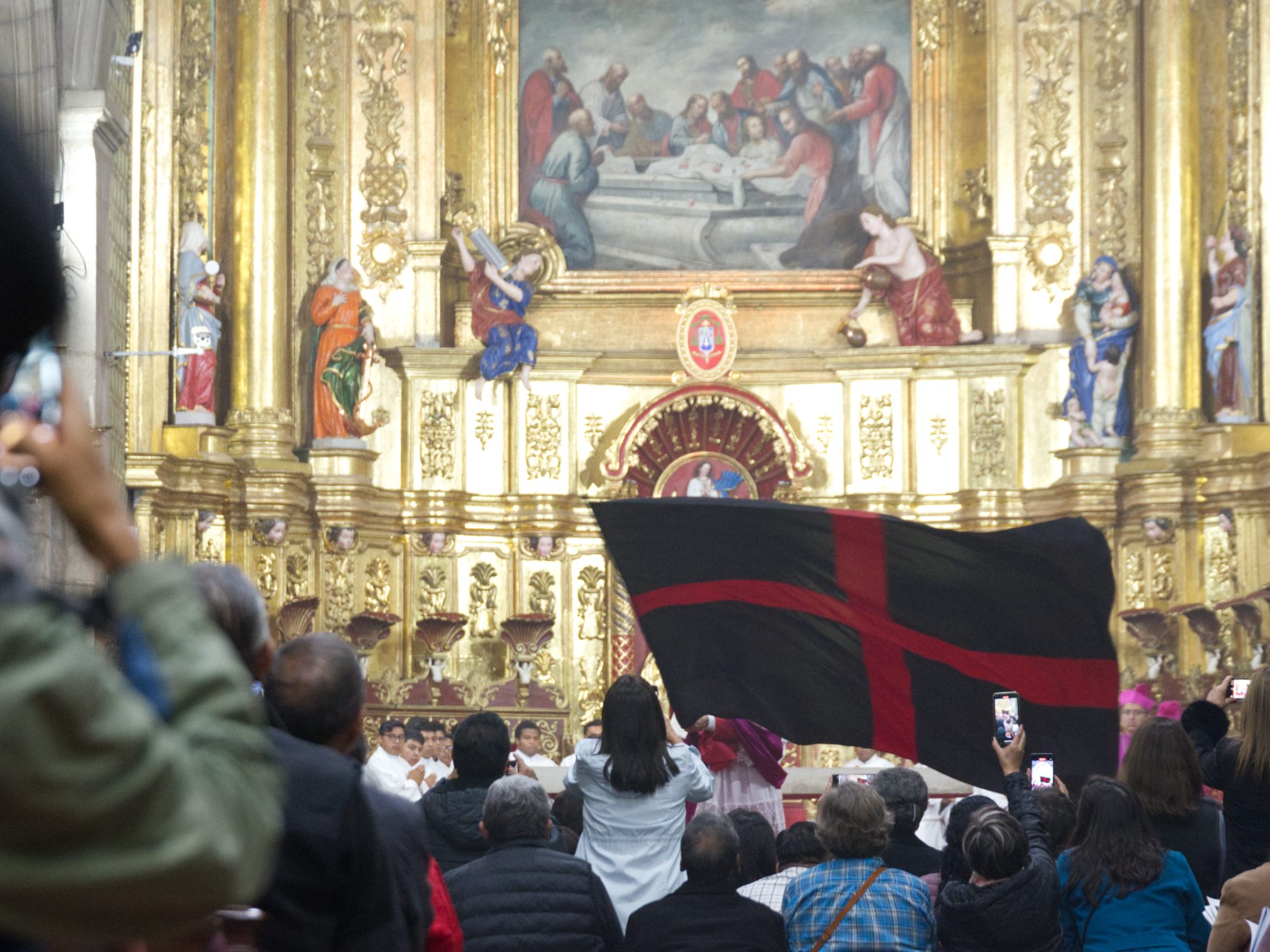 A flag with a red cross on black background is waved across the prostrate bodies of priests (not seen) in Quito's City Cathedral for Arrastre de Cuadas