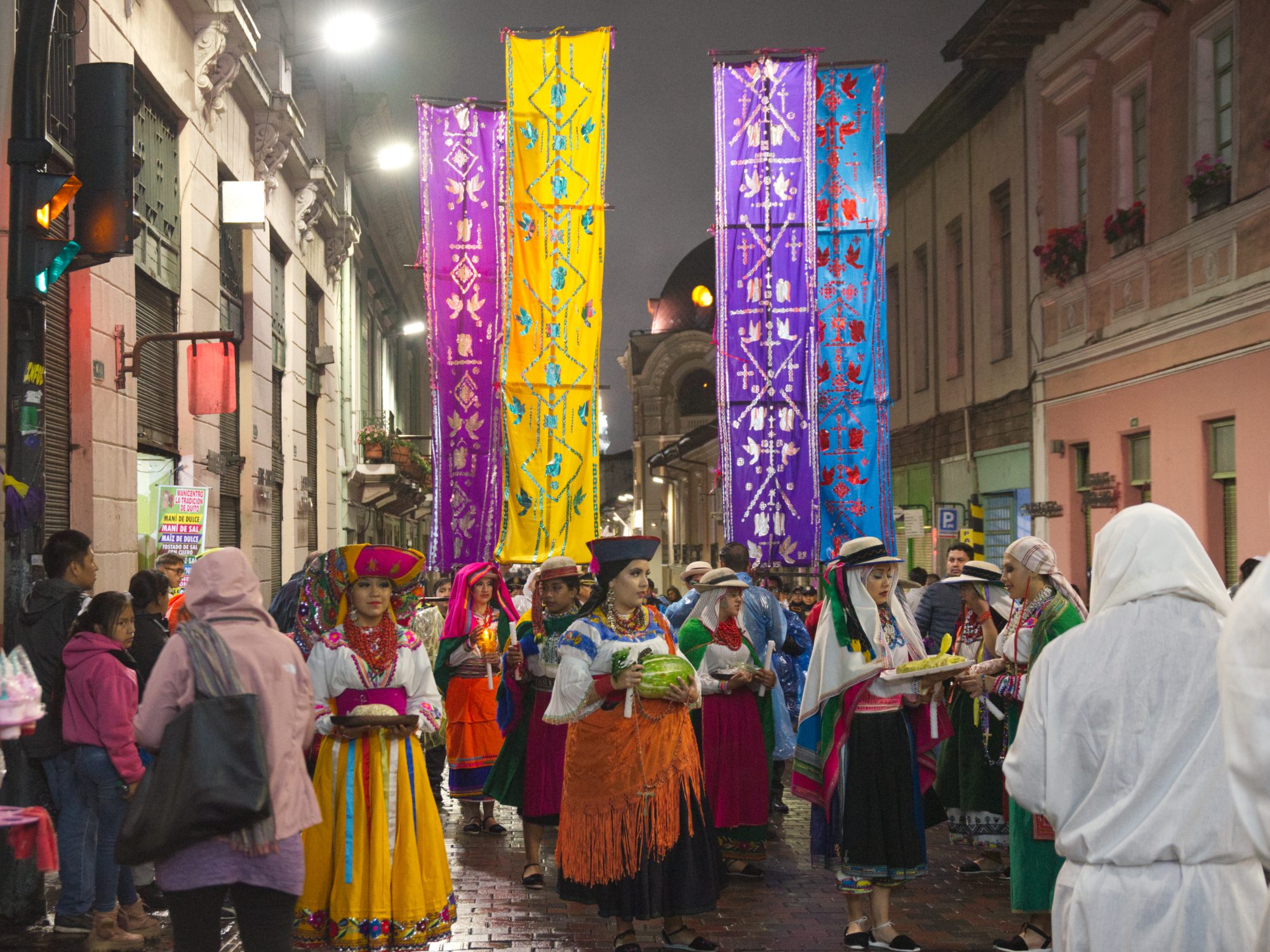 An evening procession on the historic streets of Quito with women dressed in traditional costume holding colorful banners