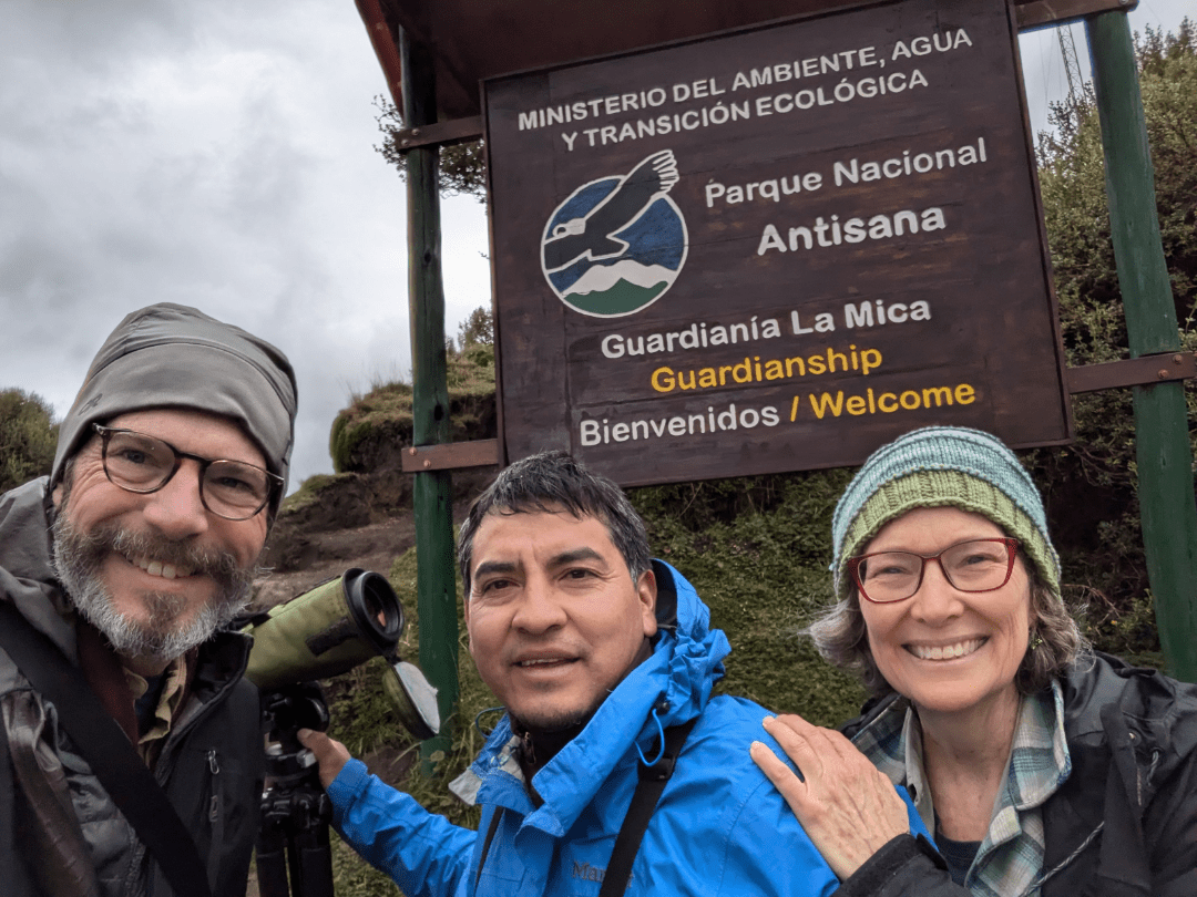 Three people stand in front of a sign for Antisana National Park