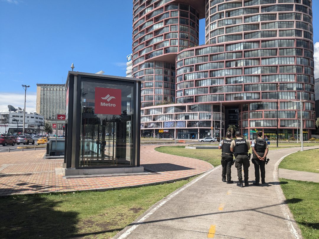 Three police officers stroll by the elevator entrance of the Carolina Metro Station in Quito, Ecuador