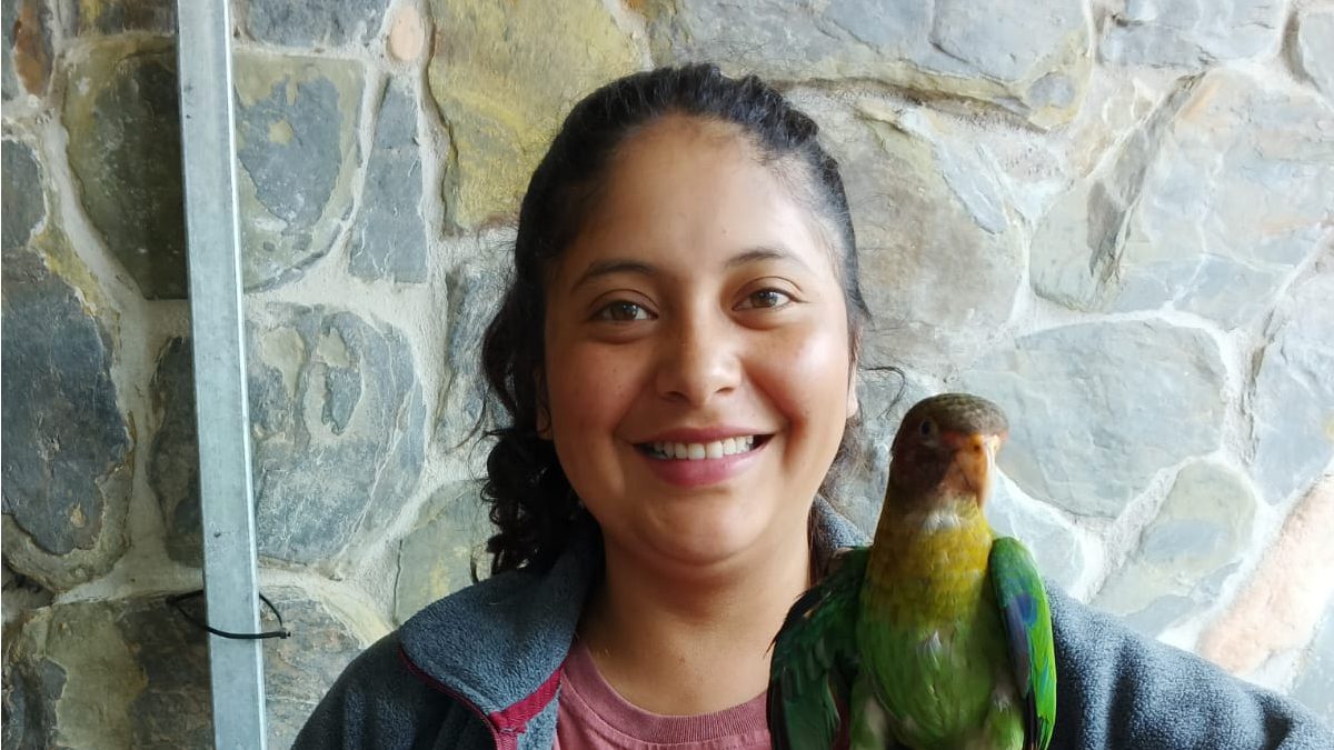 Laura Gualco smiles for the camera while a Rose-cheeked Parrot perches on her finger
