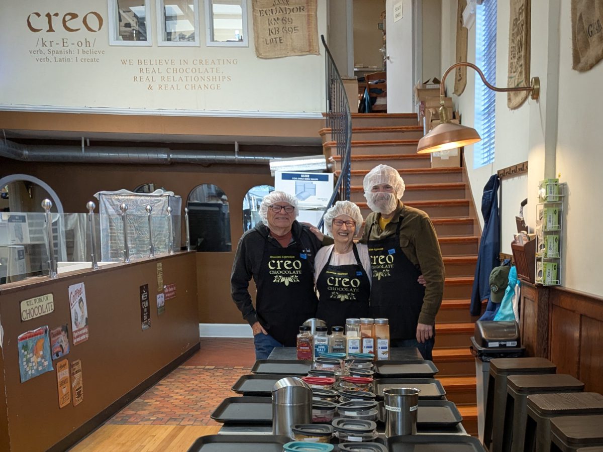 Parents and Scott at Creo Three people stand at the end of a long prep table, dressed in Creo apprentice aprons, hair nets and a beard net for one gentleman.