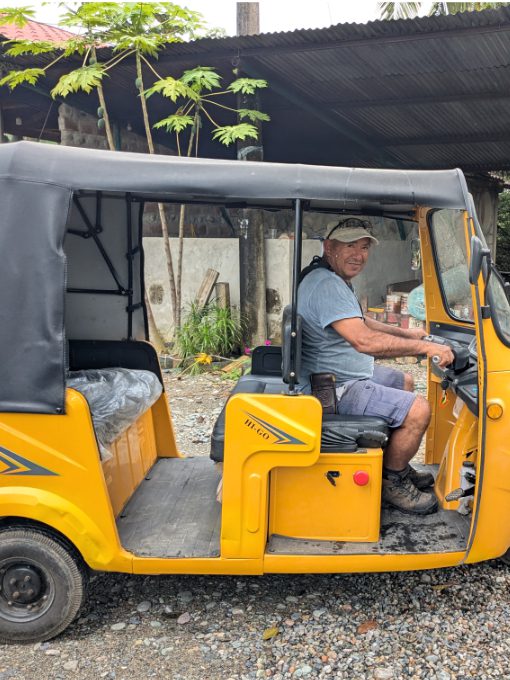 Jiovany sits in a bright yellow electric tricycle, made to transport about 4-5 people, including the driver.
