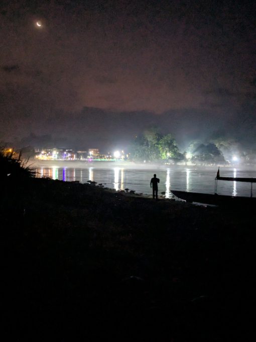 A man and a motor canoe are silouetted by the bright lights of Puerto Misahualli reflecting off the Napo River
