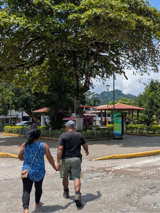 A couple holding hands crosses the street towards the Puerto Misahuallí central plaza