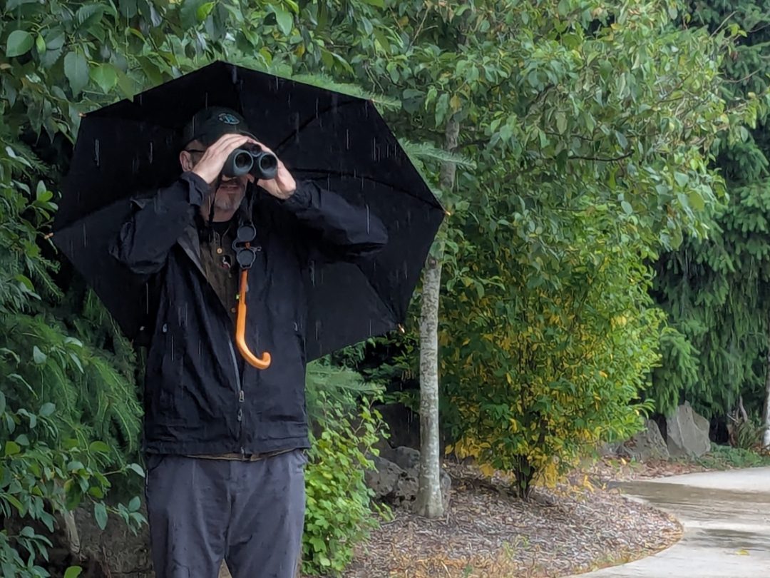 Scott in a black raincoat holding an umbrella while using the AX Visio.