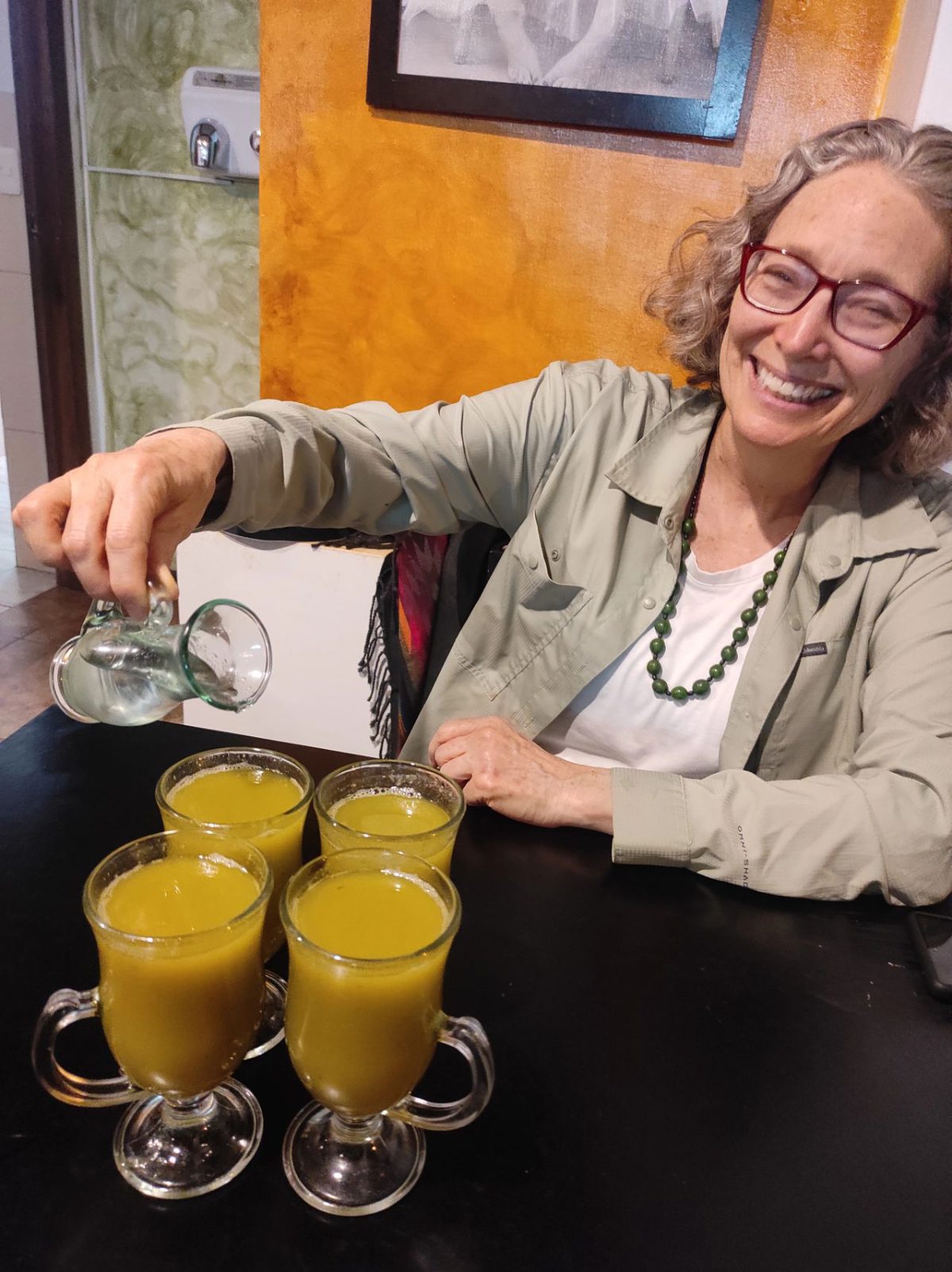 Angie pouring aguardiente into bright orange canelazos.