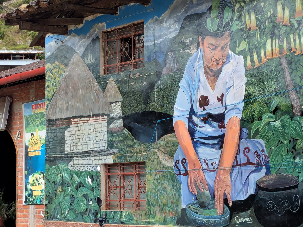 An intricate mural of a woman using a traditional mortar and pestle with Chachapoyan buldings and Laguna de los Condores in the background