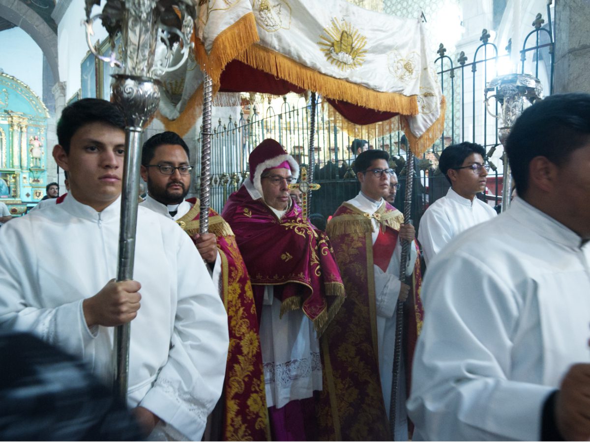 Archbishop beneath ceremonial canopy holding jeweled cross relic during Arrastre de Caudas in Quito