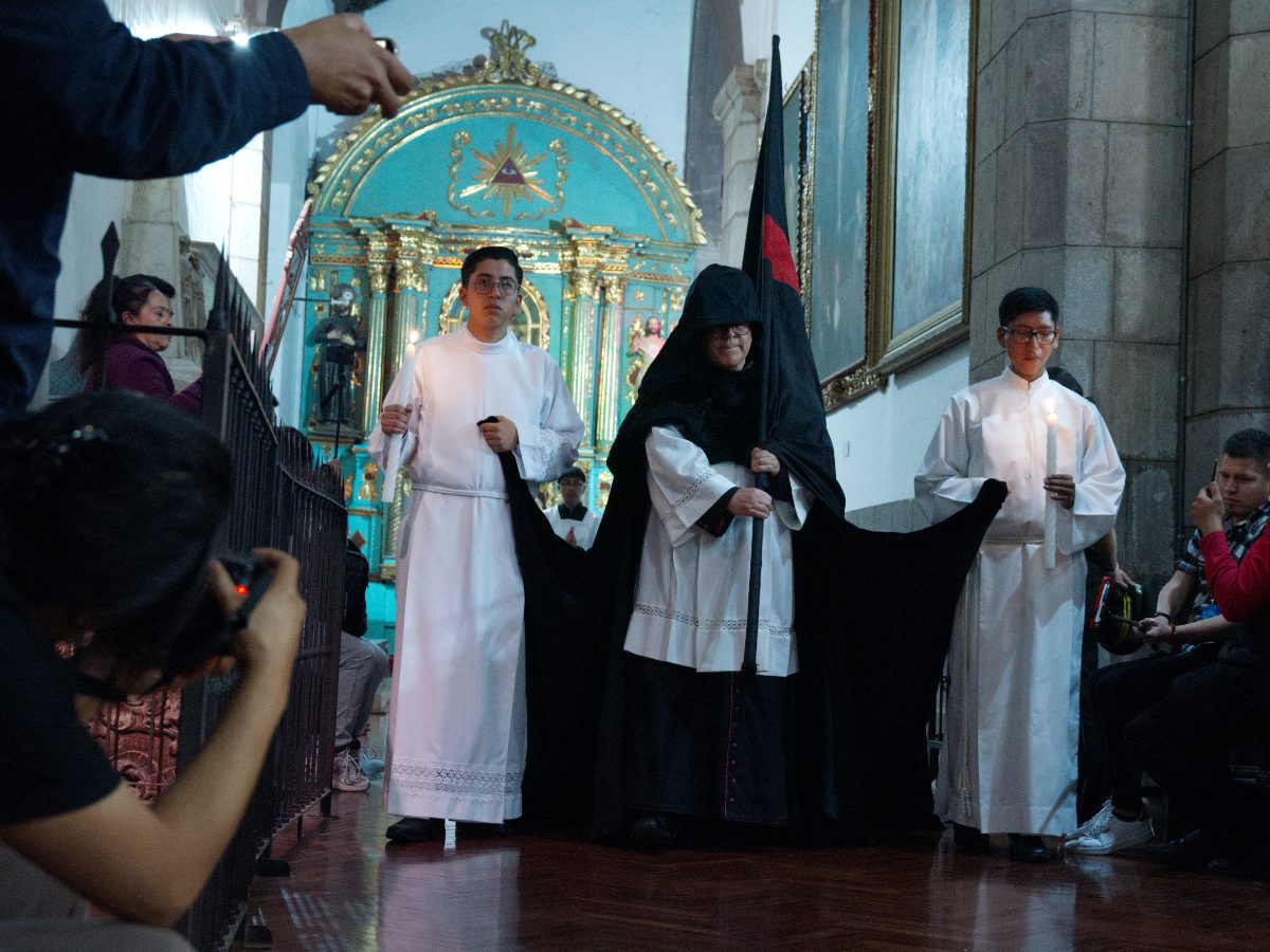 Canon carrying large black flag with red cross, escorted by acolytes, Arrastre de Caudas procession Quito