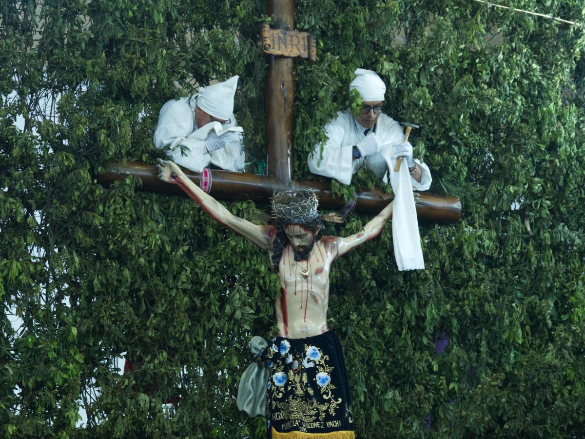Two men dressed completely in white prepare to remove a wooden statue of Jesus from the cross.