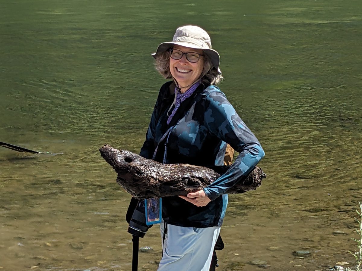 Angie holds a waterlogged piece of wood shaped like a river otter