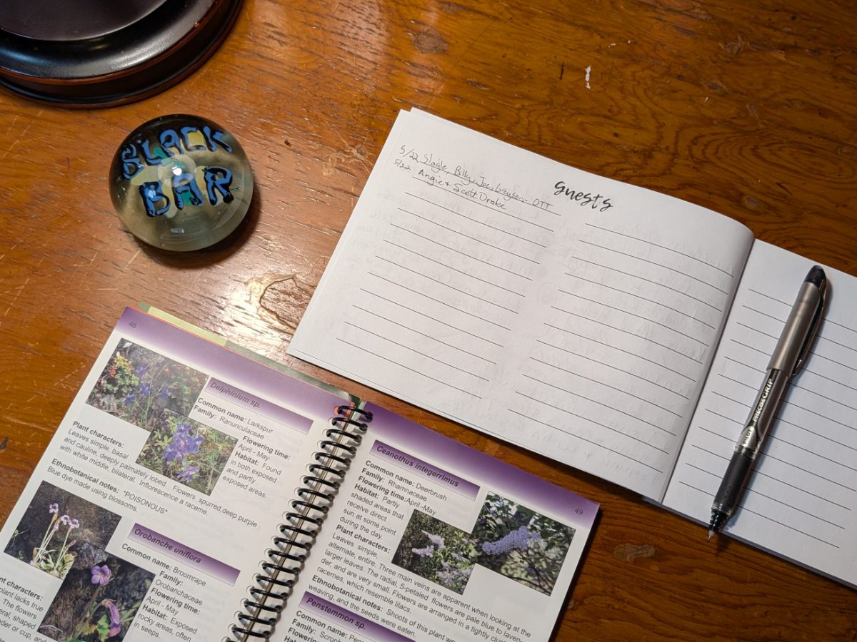 A guest book, a paperweight with the words Black Bar in blue and black glass, and a wild flower identification book