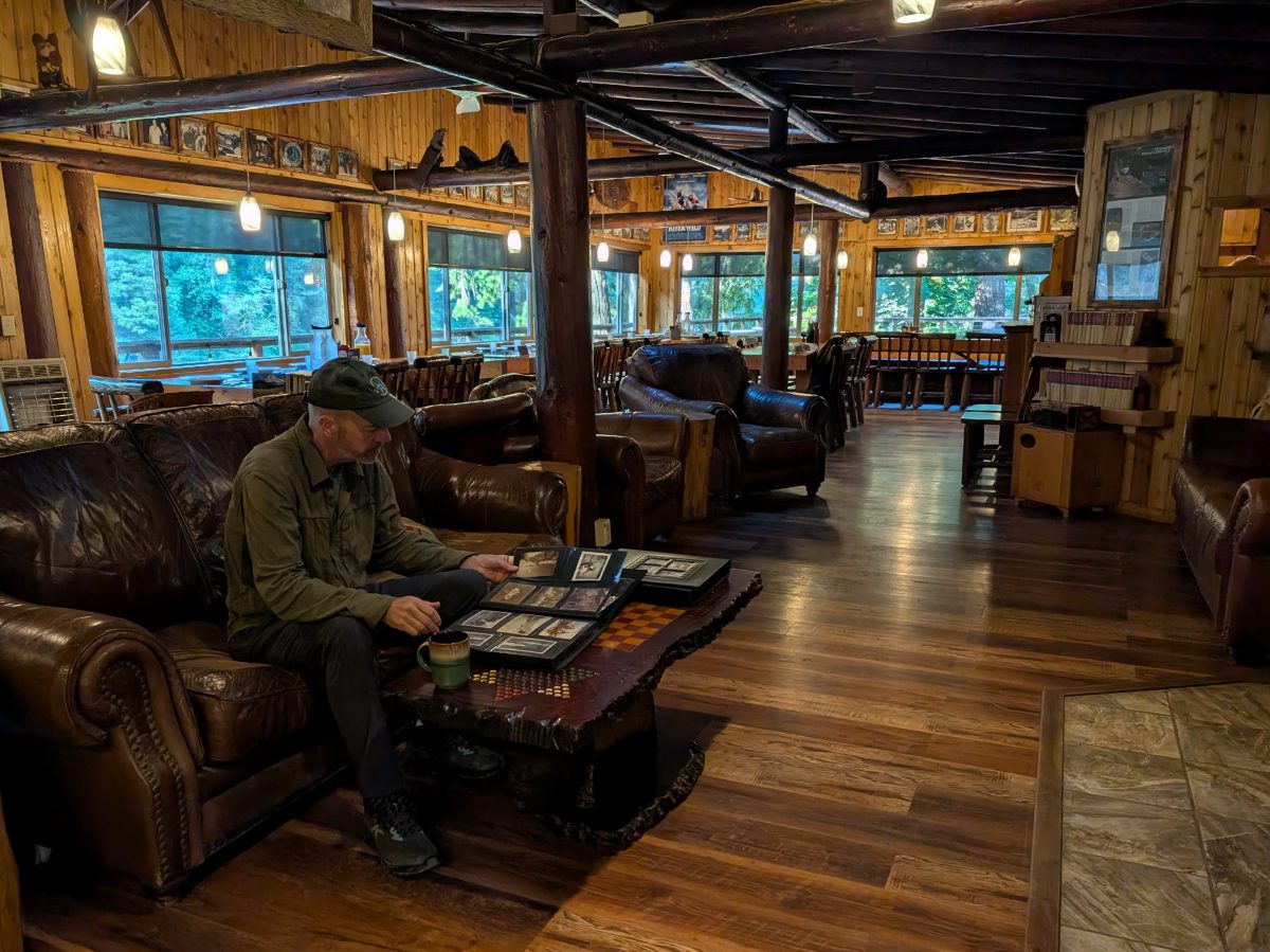 Scott sits on a leather couch looking at a photo album in the dining room, sitting area of Paradise Lodge.