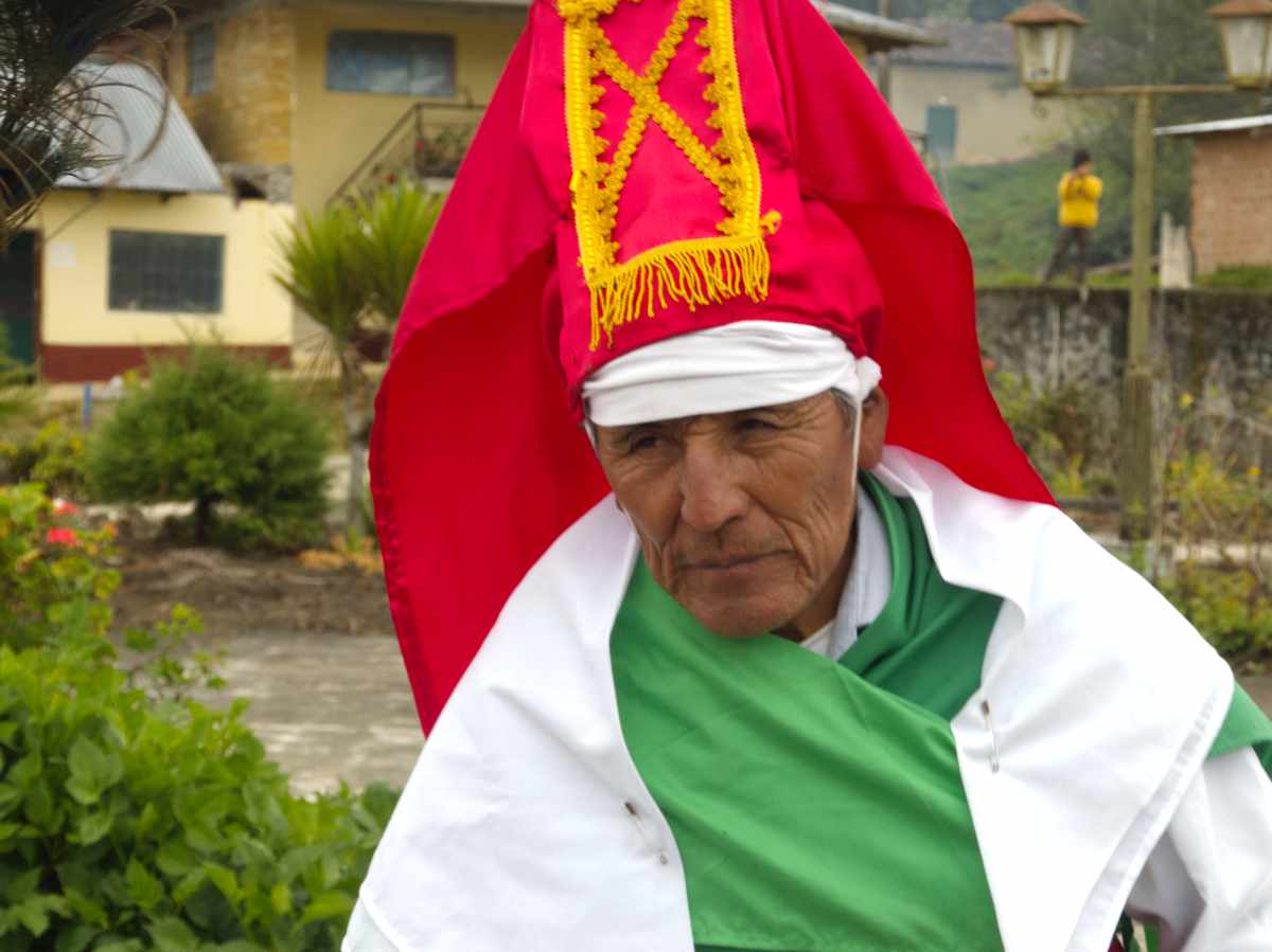 Elder Chuquiaj dancer in Cuemal, Peru, close-up portrait showing his tall, ribboned headdress and calm expression.