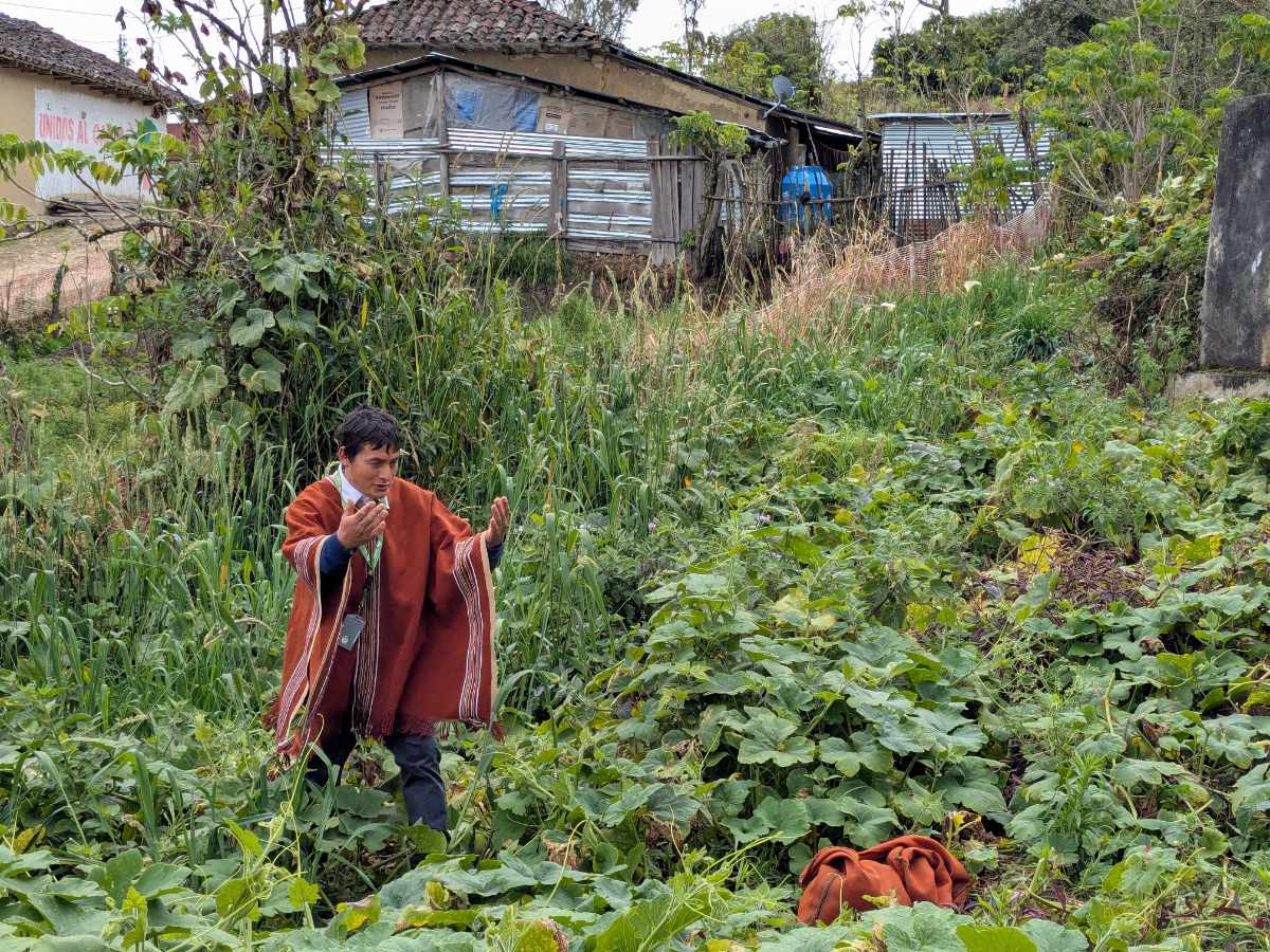 Dagoberto in his rust colored poncho narrates the story of the Chuquiar while standing near the spring in a field full of squash and sessile joyweed.
