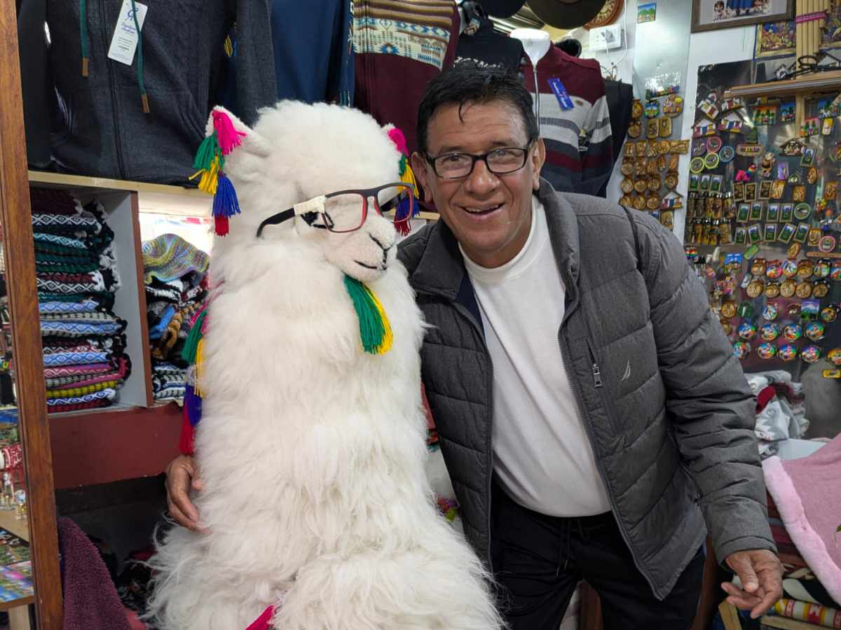 Un hombre con gafas y una chaqueta acolchada abraza a una llama disecada de tamaño real y sonríe para la cámara.