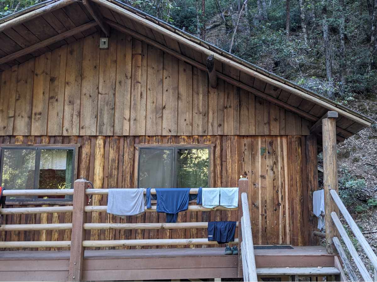 Clothing hanging out to dry on the railing of the front porch of a rustic cabin.