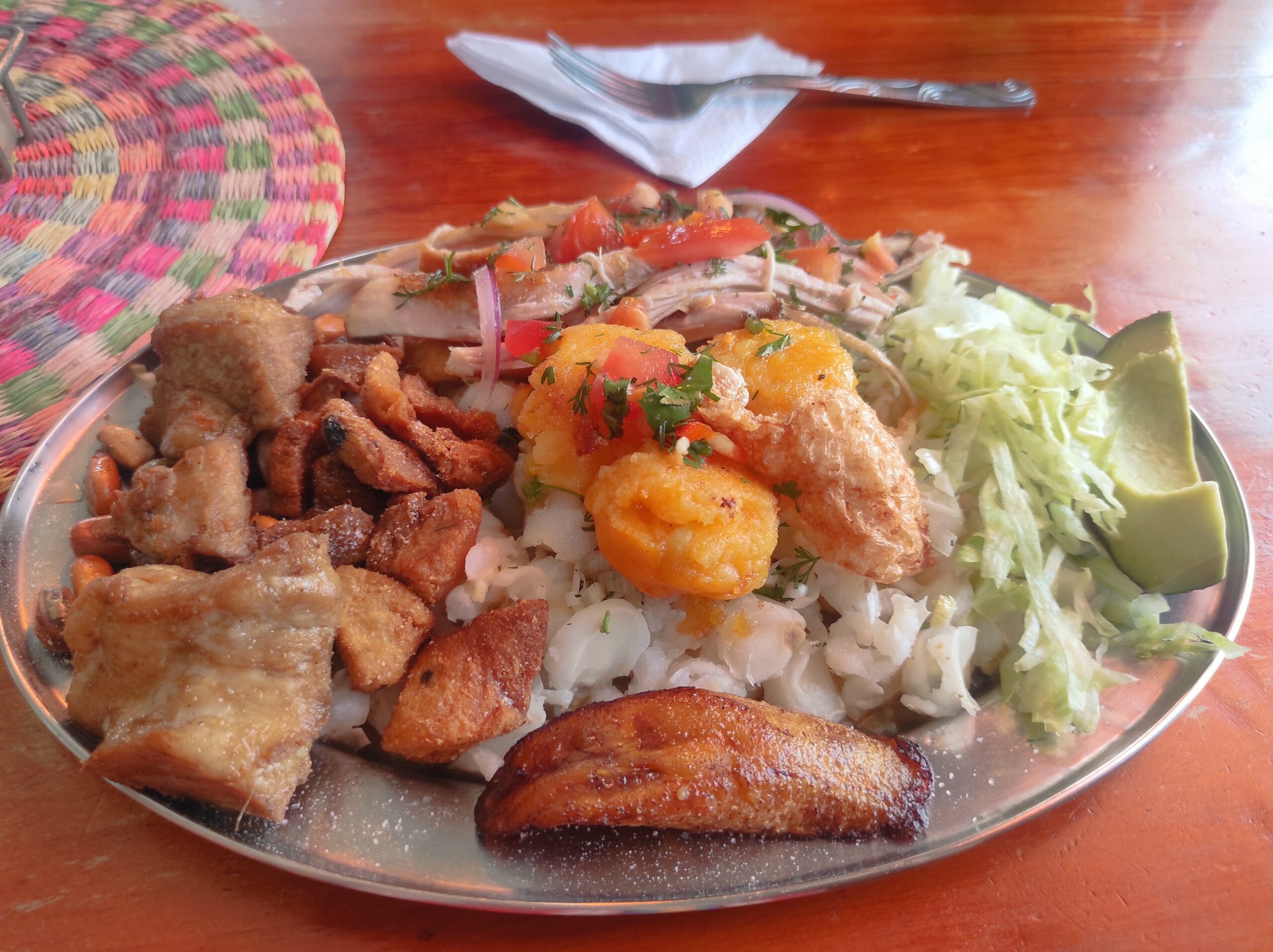 Un plato de hornado pastuso al estilo ecuatoriano, cerdo asado acompañado de guarniciones como mote, plátano maduro y llapingachos.<br/><br/>