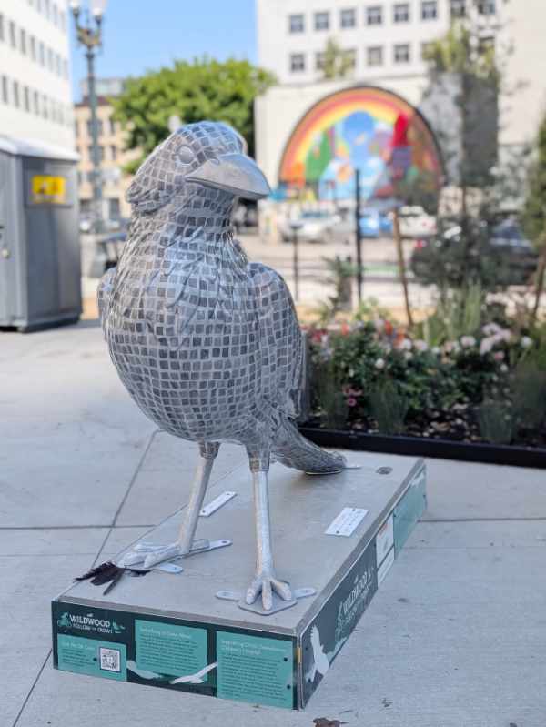 Mirroball Messenger, a crow sculpture in Darcelle XV Plaza, a colorful rainbow mural in the background. 