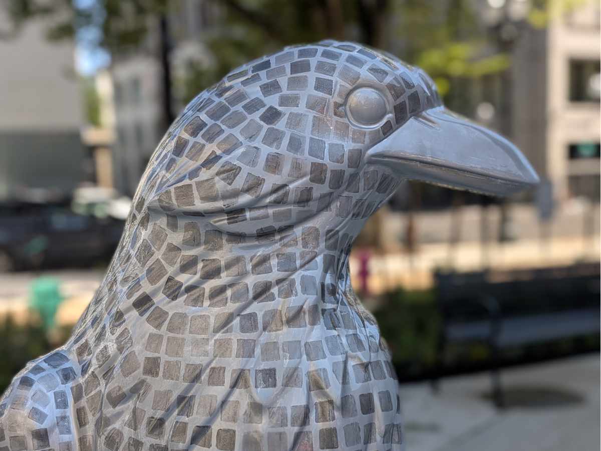 A crow sculpture painted in silver with dark gray squares lined up like tiles on a disco ball.